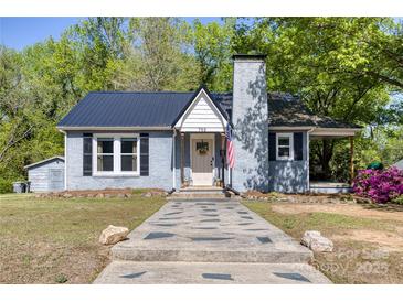 Charming one-story home with a black metal roof, brick chimney, landscaped yard, and inviting front entrance at 702 Hazel Ave, Kannapolis, NC 28083