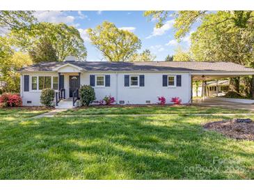 Charming, one-story home with white brick, dark shutters, covered carport and a lush, green lawn at 706 Lowell Ave, Lowell, NC 28098