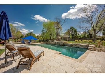 Inviting backyard pool with stone surround, outdoor fireplace, and lounge chairs offers a relaxing oasis at 12932 Westmoreland Farm Rd, Davidson, NC 28036