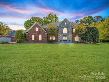 Beautiful brick and stone home with lush lawn and manicured landscaping under a picturesque sunset sky at 3677 Antioch Church Rd, Matthews, NC 28104