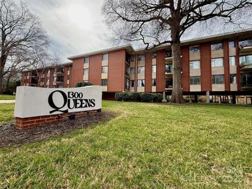 Brick condo building with '1300 Queens' sign, lawn, and mature trees creating a welcoming exterior view at 1300 Queens Rd # 210, Charlotte, NC 28207