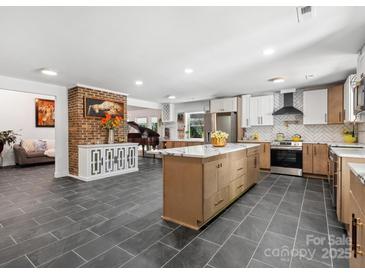 Spacious kitchen with gray tile floors, brick accent wall, island, white cabinets and stainless steel appliances at 6724 Brushwood Dr, Charlotte, NC 28262