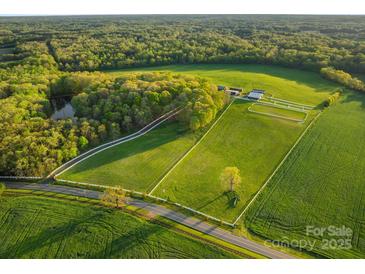 An aerial view of a horse farm with green pastures, a pond, stables, and mature trees surrounding the property at 15670 Bethel Avenue Ext, Midland, NC 28107