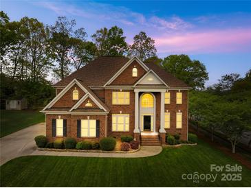 Elegant brick home with a manicured lawn and classic architectural details at twilight at 130 Weeping Spring Dr, Mooresville, NC 28115