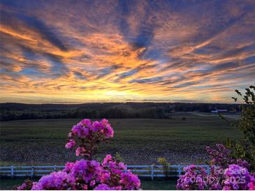 Breathtaking sunset view over the open fields with pink flowers in the foreground and a white picket fence at 44392 Dennis Rd, Albemarle, NC 28001