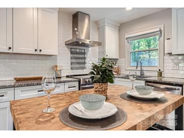 Bright kitchen featuring white cabinets, subway tile backsplash, stainless steel range hood, and butcher block island at 1702 Herrin Ave, Charlotte, NC 28205