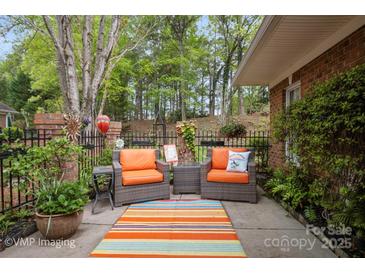 Relaxing patio with orange cushioned seating, potted plants, and beautiful green surroundings at 7444 Hurstbourne Green Dr, Charlotte, NC 28277