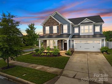 Charming two-story home showcasing stone accents, blue siding, lush landscaping, and a two-car garage at 12710 Es Draper Dr, Huntersville, NC 28078