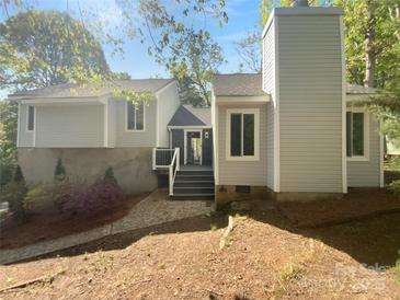 View of the home with light grey siding and stone foundation, accented by lush landscaping at 8000 Briardale Dr, Charlotte, NC 28212