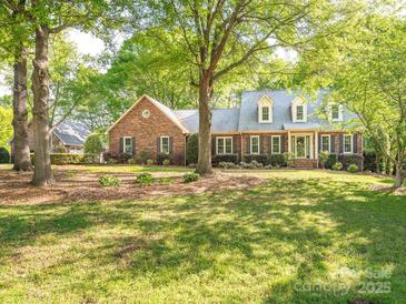 Charming brick home featuring dormer windows, mature trees, and a beautifully landscaped front yard at 3815 Glen Haven Sw Dr, Concord, NC 28027
