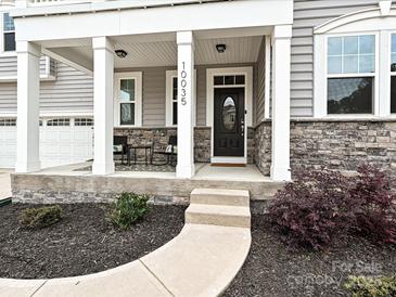 Inviting front porch with stone accents, white columns, and a cozy seating area, providing a welcoming entrance at 10035 Mast Cove Ln, Charlotte, NC 28278