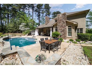 Beautiful backyard with pool, stone fireplace, and outdoor dining area surrounded by lush greenery at 114 Misty Meadows Ct, Mooresville, NC 28117