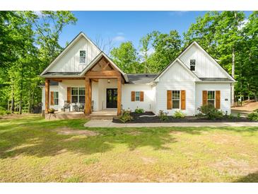 Charming white farmhouse with a wood-accented porch and shutters surrounded by lush greenery at 358 Grassy Ridge Ct, Clover, SC 29710
