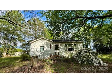 Cozy single story home with white siding and a small porch surrounded by lush greenery and flowers at 2118 Polkville Rd, Shelby, NC 28150