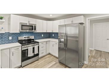 Modern kitchen featuring stainless steel appliances, white cabinets, and a stylish blue tiled backsplash at 109 W Poplar St, Stanley, NC 28164