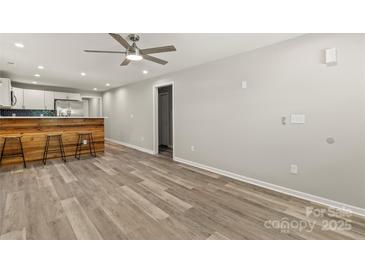 Spacious living room with wood-look flooring, ceiling fan, and bar area open to the modern kitchen at 109 W Poplar St, Stanley, NC 28164