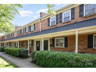 Charming brick townhome with a covered front porch, lush landscaping, and classic black shutters at 1218 Green Oaks Ln # E, Charlotte, NC 28205