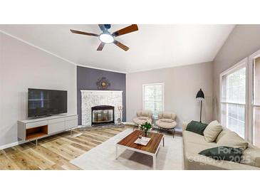 Cozy living room featuring a brick fireplace, ceiling fan, and light colored wood flooring at 1274 Oakbrook Ln, Denver, NC 28037
