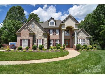 Beautiful brick and stone home with a manicured lawn, mature trees, and a winding walkway to the front door at 6927 Ellington Farm Ln, Mint Hill, NC 28227