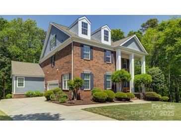 A brick two-story home with blue shutters, dormer windows and a driveway, surrounded by green trees and landscaping at 9810 Daufuskie Dr, Charlotte, NC 28278