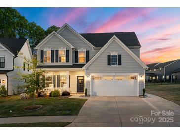Charming two-story home featuring a manicured lawn, gray siding, black shutters and a two car garage under a vibrant sunset at 1543 Ab Moore Jr Dr, Indian Trail, NC 28079