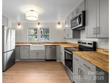 Well-lit kitchen with stainless steel appliances, wooden countertops and gray cabinets at 300 N Ervin Ave, Newton, NC 28658