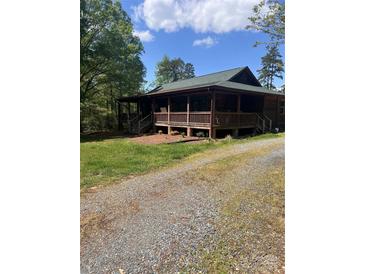 Charming cabin-style home with a large covered porch and gravel driveway surrounded by lush greenery and trees at 9751 Quail Run Rd, Locust, NC 28097