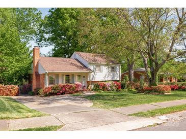 Charming home with a brick chimney, colorful flower beds, and a spacious front yard surrounded by mature trees at 1114 Hartford Ave, Charlotte, NC 28209