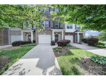 Charming brick townhome featuring an attached garage, well-maintained lawn, and mature trees at 9862 Walkers Glen Nw Dr, Concord, NC 28027