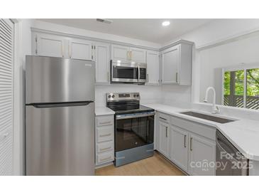 Updated kitchen features stainless steel appliances, gray cabinets with gold pulls, and granite countertops at 6523 Clavell Ln, Charlotte, NC 28210