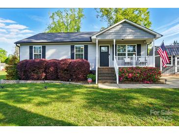 Charming home with a well-manicured lawn and a cozy front porch decorated with flowering bushes and an American flag at 303 Caroline Ave, Lowell, NC 28098