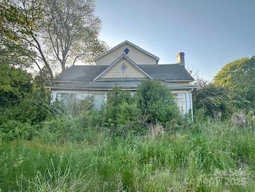 Two story home with gable roof and sunroom is surrounded by overgrown landscaping at 6000 S Main St, Salisbury, NC 28147