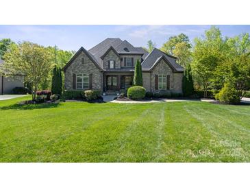 Charming stone facade home featuring mature trees, lush landscaping, and a well-manicured lawn at 15909 Heath Aster Way, Davidson, NC 28036