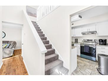 Bright staircase featuring carpeted stairs, white walls, and direct access to a modern kitchen space at 7407 Mystic Ln, Charlotte, NC 28227