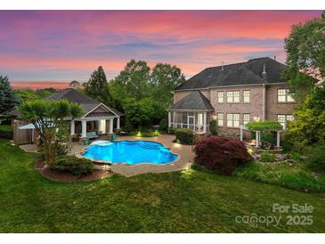 A luxurious backyard showcasing a large in-ground pool, well-manicured lawn, and beautiful landscaping with a house in the background at 2304 Thunder Gulch Ct, Waxhaw, NC 28173