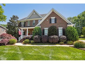 Charming brick home with a covered front porch, lush landscaping, and a well-manicured lawn at 10716 Persimmon Creek Dr, Mint Hill, NC 28227