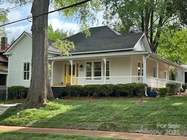 Charming white home with a welcoming front porch, a lush green lawn, and vibrant trees at 300 Kelly St, Statesville, NC 28677