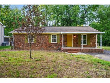 Charming brick home with a covered porch, yellow front door, green shutters, and mature landscaping at 6558 Covecreek Dr, Charlotte, NC 28215