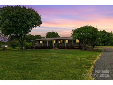 Charming ranch-style home with a well-manicured lawn and mature trees under a colorful sunset at 6813 Rebel Rd, Marshville, NC 28103