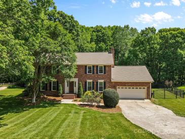 Traditional brick home featuring an attached garage, well-manicured lawn, and mature trees at 16565 Kimbolten Dr, Huntersville, NC 28078