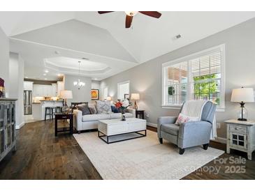 Bright living room features hardwood floors, a tray ceiling, and a view into the kitchen at 8473 Bing Cherry Dr, Denver, NC 28037