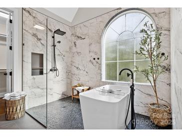 Bright bathroom featuring marble walls, black pebble tile, soaking tub and glass shower with a rainfall shower head at 18730 Floyd Ct, Davidson, NC 28036