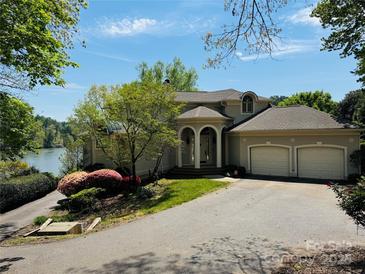 Beautiful beige home featuring a two-car garage, arched entryway, lush landscaping, and partial lake view at 255 Charlotte Ann Ln, Hickory, NC 28601