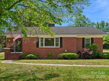 Charming one-story brick home featuring a well-maintained lawn and mature landscaping, American flag near entry at 613 W Pine St, Kershaw, SC 29067