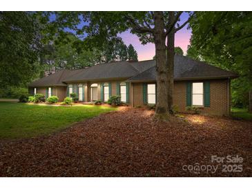 Charming brick home with green shutters, a lush lawn and mature trees at dusk at 8368 Fairfield Forest Rd, Denver, NC 28037