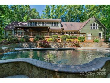 View of a large pool and stone patio area that backs up to the house with lots of shrubbery and foliage at 8400 Prince Valiant Dr, Waxhaw, NC 28173