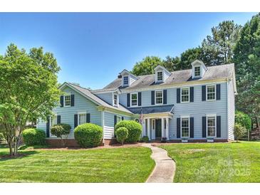 Charming two-story home with a well-manicured lawn, black shutters, and a classic American flag at 9209 Cameron Wood Dr, Charlotte, NC 28210