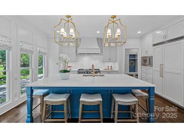 Bright kitchen features a large island with marble countertops, custom cabinets and gold light fixtures at 17924 River Ford Dr, Davidson, NC 28036