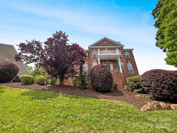 Two-story brick home with a balcony, beautiful landscaping, and healthy trees on a lush green lawn at 3904 Hounslow Ln, Harrisburg, NC 28075