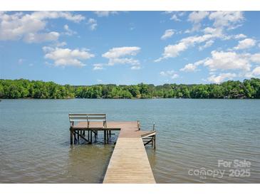 Lake view featuring a wooden dock extending into the water with a bench, against a backdrop of a clear blue sky at 4960 Longfield St, Claremont, NC 28610